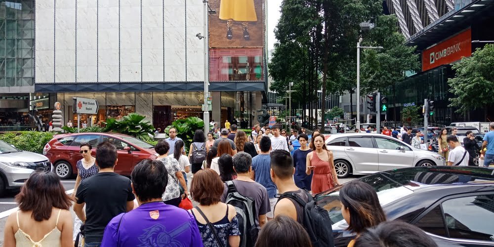 A bustling street in Singapore filled with a diverse crowd of people walking and engaging in daily activities.