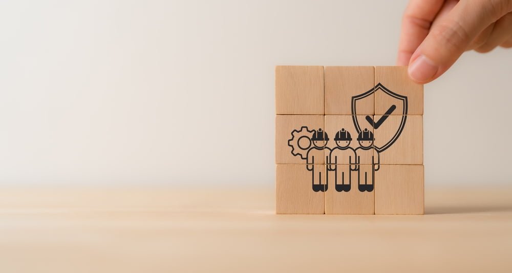 A person holds a wooden block featuring an image of three construction workers alongside a shield, symbolizing Singapore Construction Safety Standards.