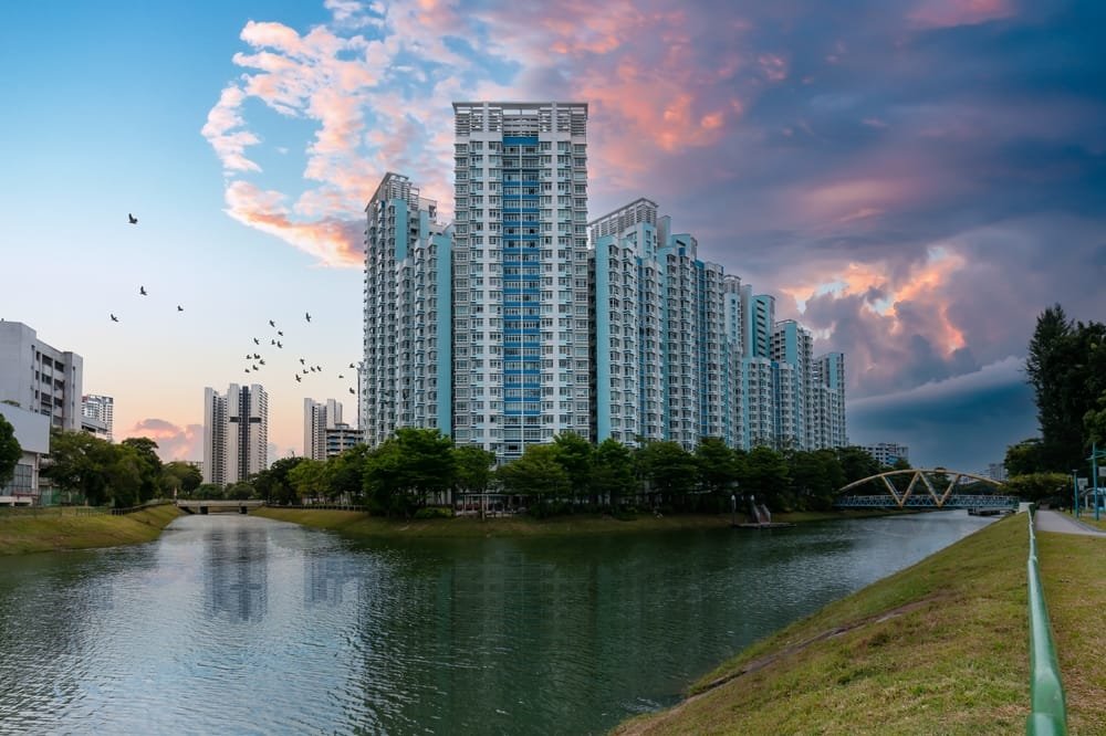 HDB Estate at Bendemeer, Singapore. High-rise buildings by a river at sunset with colorful clouds and flying birds, symbolising Affordable Housing Singapore.