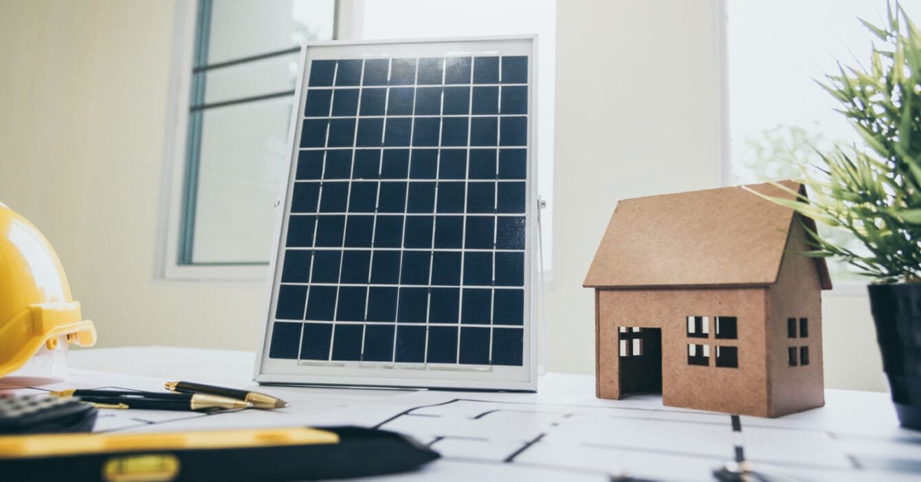 A miniature house model beside a solar panel, with construction plans and helmet on a desk, symbolising Renewable Energy in Construction Singapore.