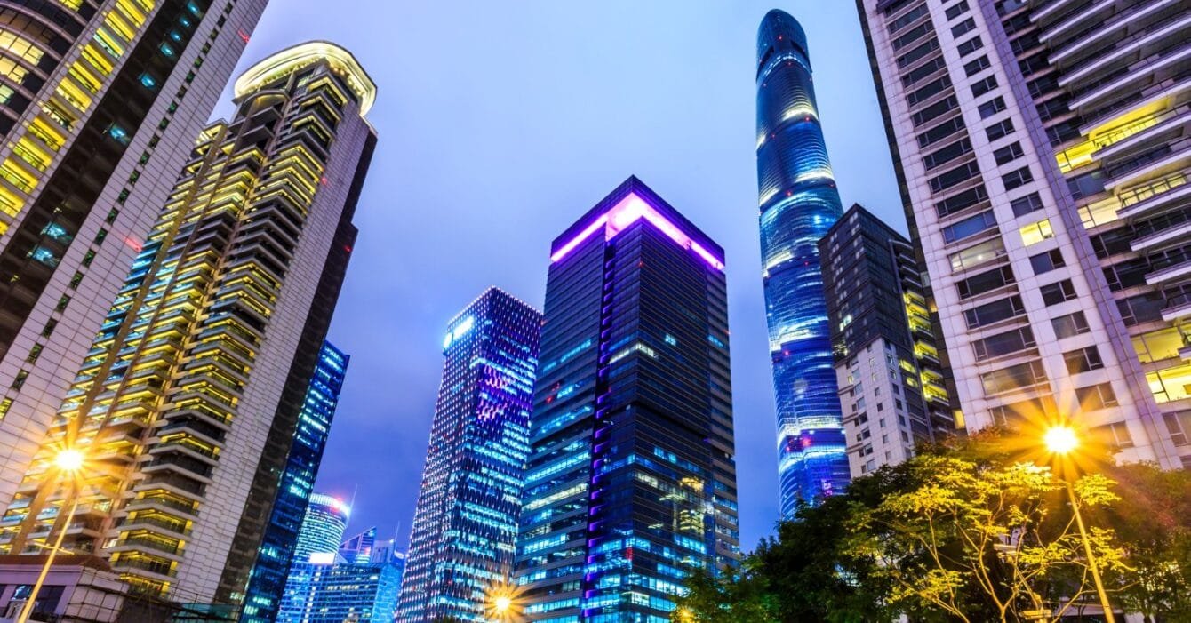 Singapore Affordable Housing Challenges: Twilight cityscape with illuminated skyscrapers and trees in the foreground.