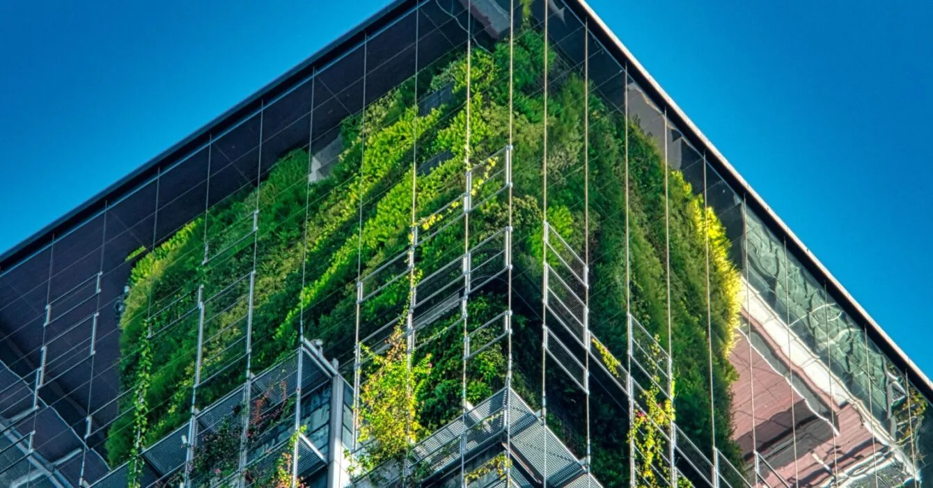 A modern building's corner features a lush green living wall, contrasted against reflective glass and a clear blue sky as Singapore Green Infrastructure Initiatives.