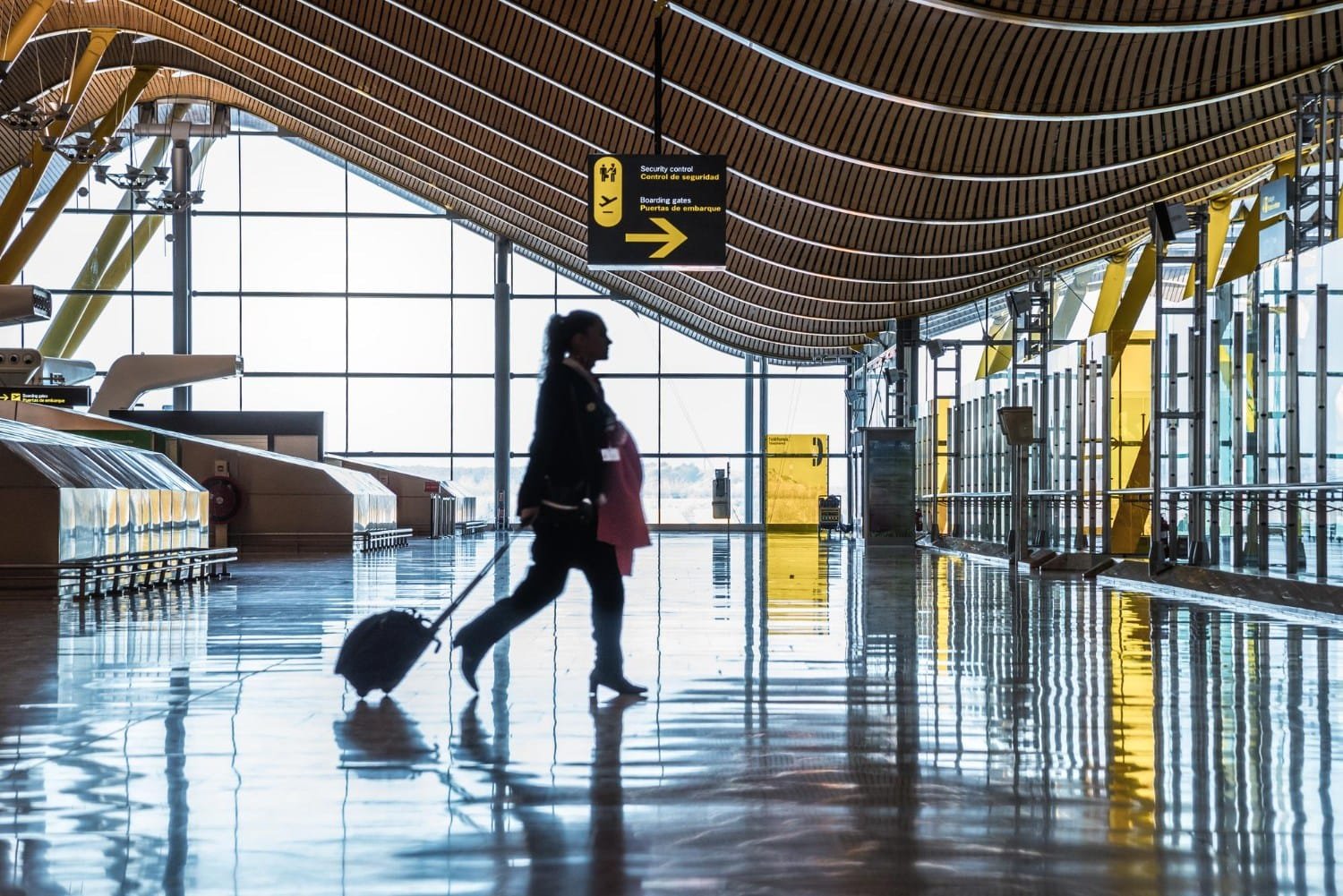 Singapore Public-Private Partnership Models represented by a traveler walks briskly through a spacious airport terminal with a striking wooden ceiling and smooth reflective floors.